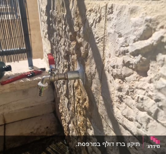 ברז מים מותקן על קיר אבן עם צינור